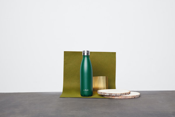 Eine grüne Isolierflasche von FLSK befindet sich auf einem Tisch zusammen mit 2 Schneidbrettchen aus Holz. FLSK Thermoskannen haben eine sehr hohe Isolation.